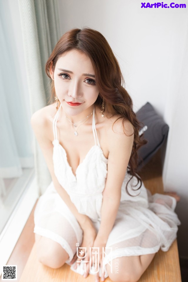 A woman in a white dress sitting on a wooden table.