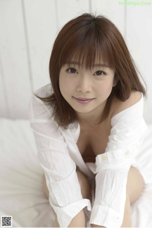 A naked asian woman sitting on a bed in a white shirt.