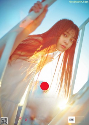 A woman with long red hair standing on a bridge.