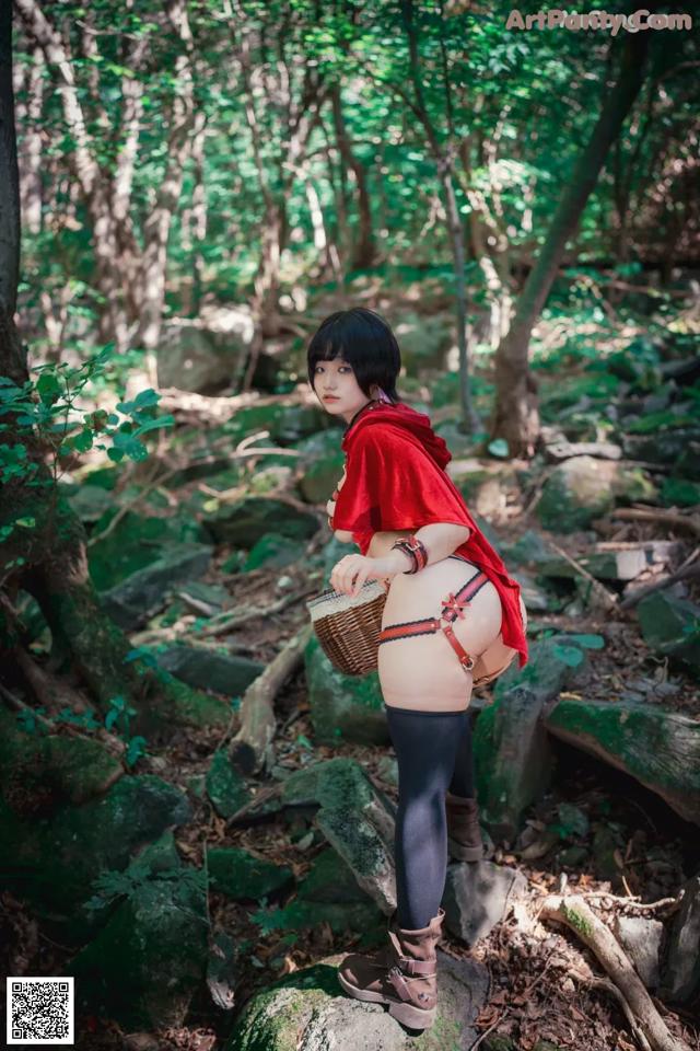 A woman in a red riding hoodie standing on a rock in the woods.