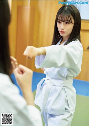 A woman in a white kimono standing on a green mat.