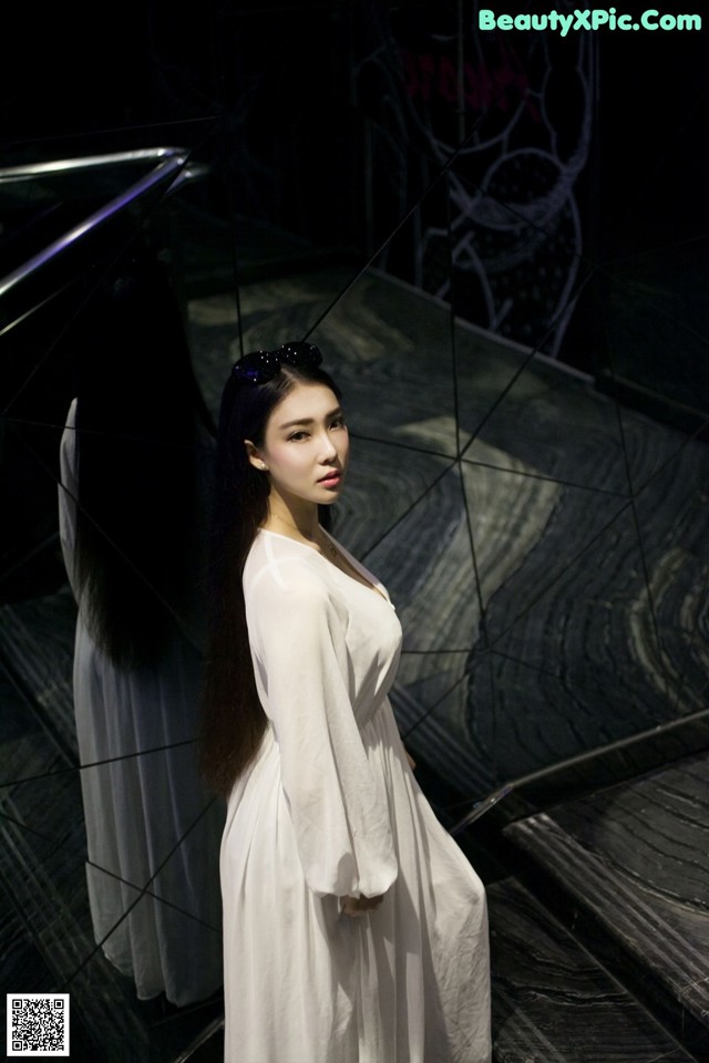 A woman in a white dress standing in front of a mirror.