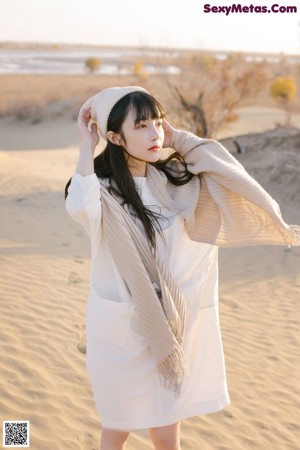 A woman in a white dress sitting on a sand dune.