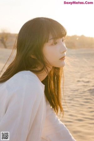 A woman in a white dress standing in the sand.