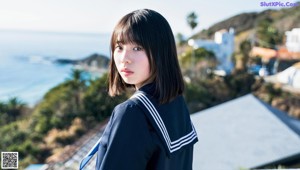 A woman in a sailor outfit sitting on a rock by the water.