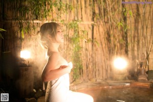 A woman in a towel standing under an umbrella.