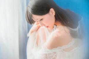 A woman in a white dress sitting on a bed.