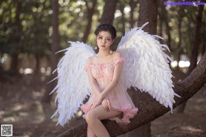 A woman in a pink dress with white wings in the woods.