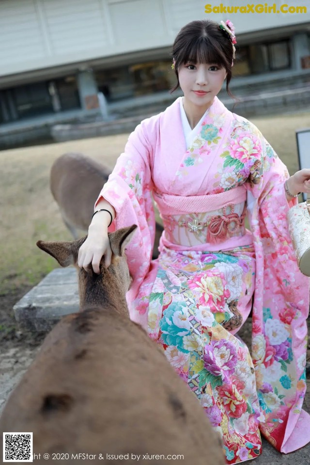 A woman in a pink kimono petting a deer.