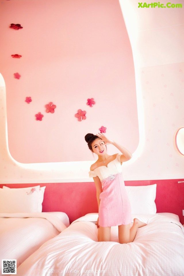 A woman in a pink dress sitting on a bed.
