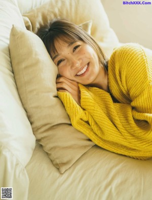 A woman in a yellow sweater is sitting on a bed.