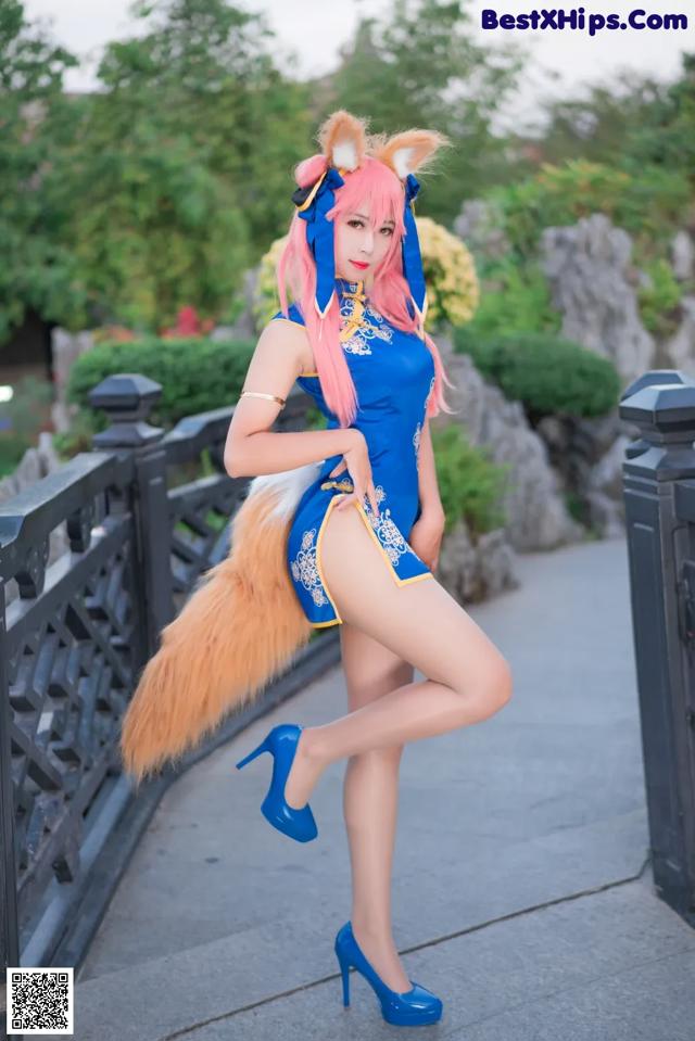 A woman in a blue dress and a fox tail posing for a picture.