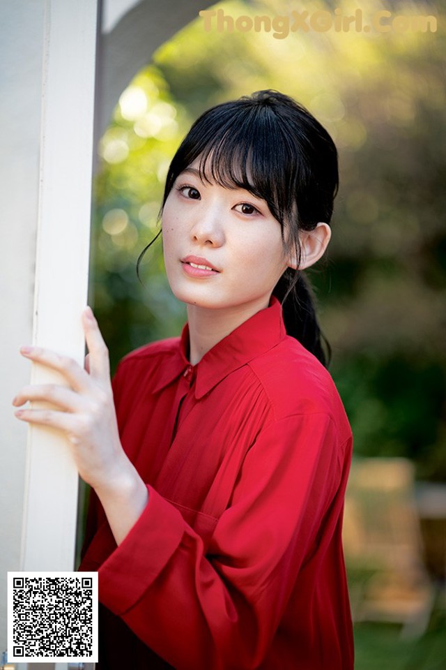 A woman in a red shirt leaning against a door.