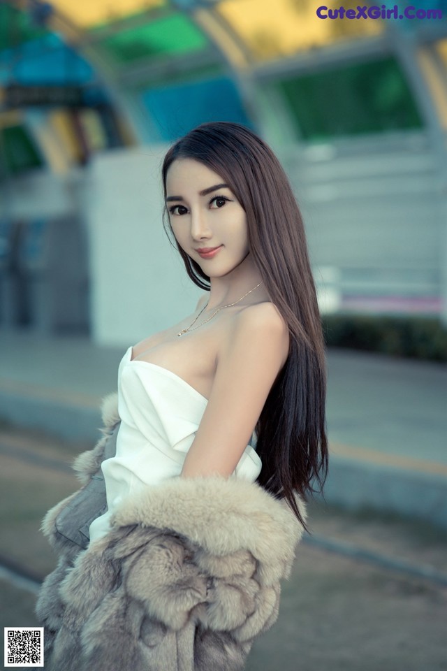 A woman in a white dress and fur coat posing for a picture.