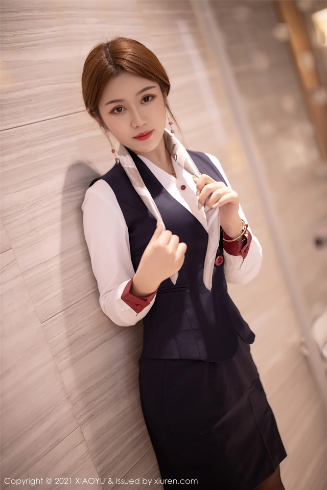 A woman in a business suit leaning against a wall.