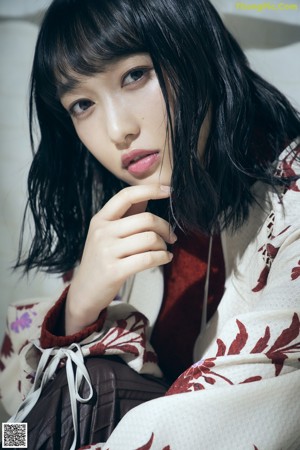 A woman in a kimono sitting on a chair with her hand on her chin.