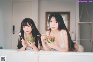 Two young women sitting on a white couch.