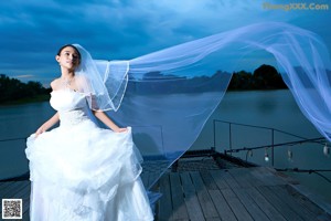 A woman in a wedding dress sitting on a dock.