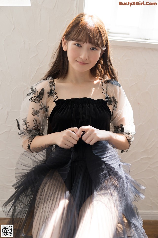 A woman in a black dress sitting on a wooden floor.